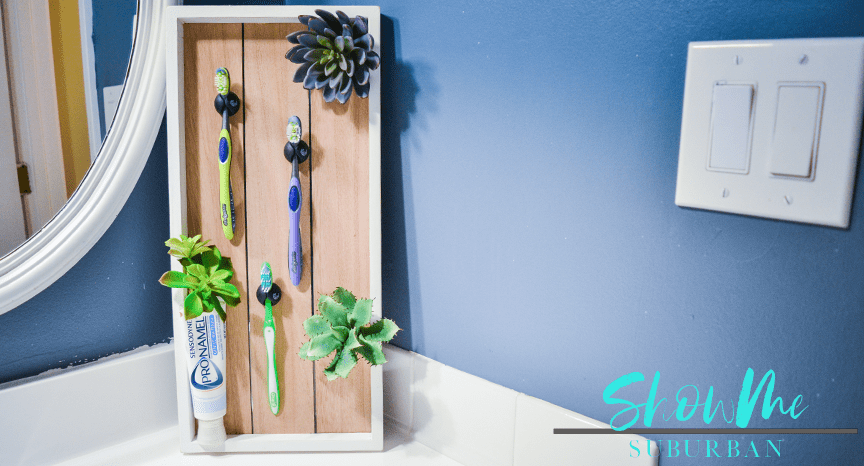 DIY toothbrush holder with toothbrushes and faux succulents | Spruce up your bathroom with this cute DIY toothbrush storage unit! This toothbrush holder helps toothbrushes dry and reduces messes. Try this quick and easy idea today. Also makes a great gift! #diydecor #organizedbathroom