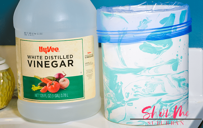 Vinegar, plastic bag, and canister with text overlay | Gross shower head? You're not alone! Here's how to clean a dirty shower head. Easily remove bacteria, mildew, and lime scale using natural ingredients you probably already have at home! #cleaning